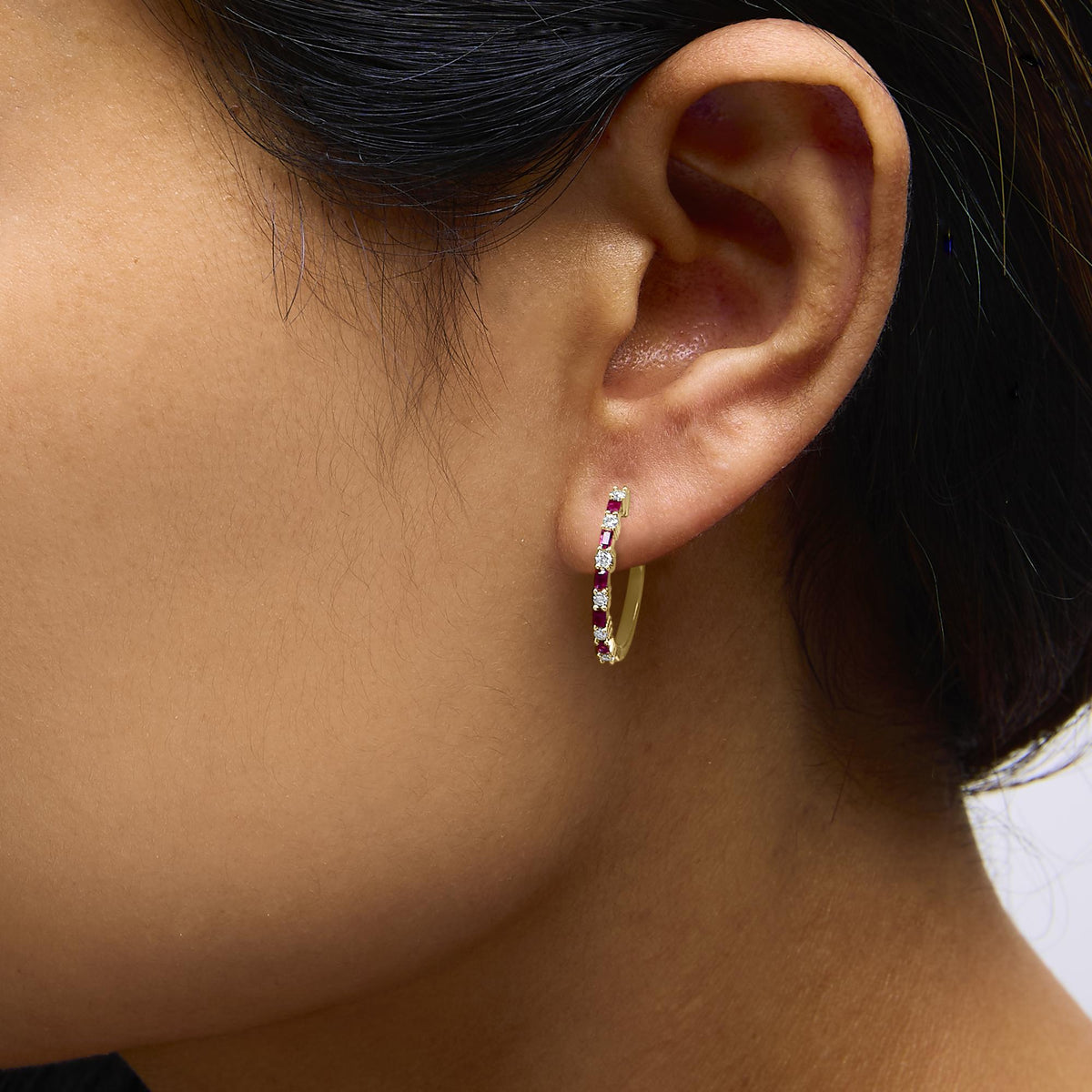 Yellow hoop earring set with alternating red baguette and white round gemstones in prong settings, shown worn on a model, close-up side angle.