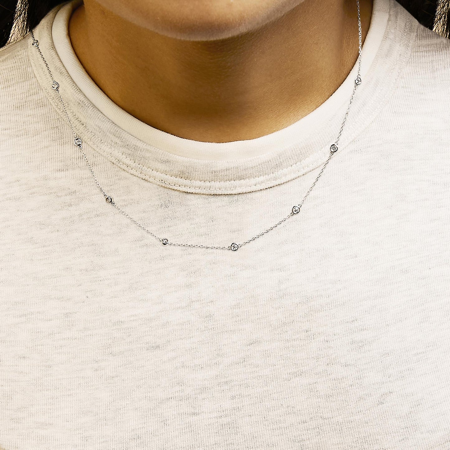 White necklace with small round white gemstones in bezel settings evenly spaced along a delicate chain, shown worn on a model, front angle.