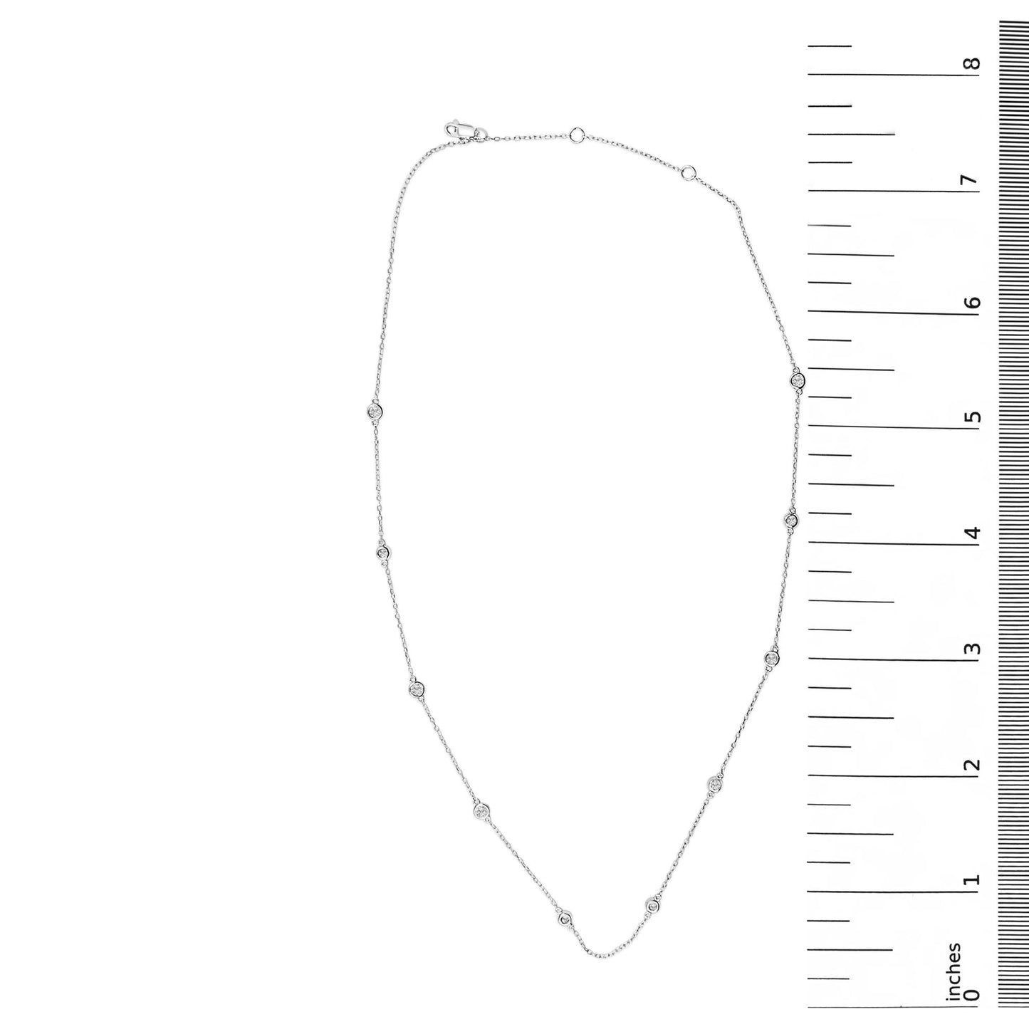 Top-down view of a white necklace with bezel-set round white gemstones evenly spaced along the chain, shown on a measurement scale.