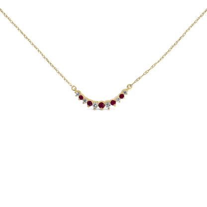 Close-up front angle of a yellow metal necklace with alternating round white and red gemstones in prong settings, shown on a white background.