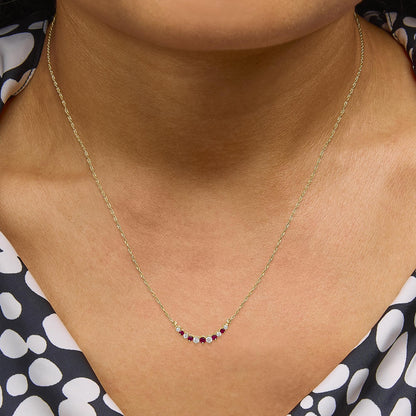 Yellow metal necklace with alternating round red and white gemstones in prong settings, shown worn on a model from a front close-up angle.