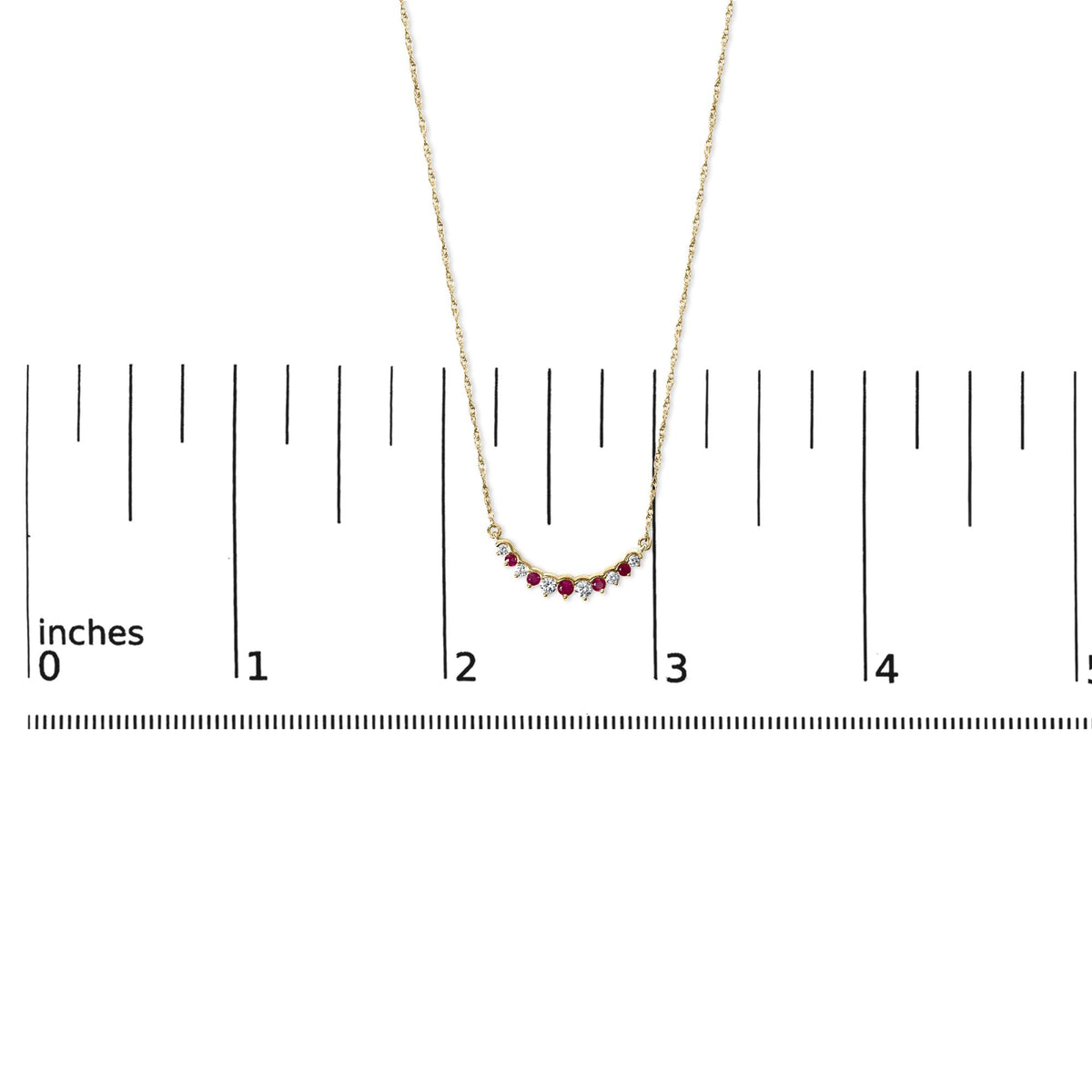 Yellow metal necklace with a curved pendant featuring round red and white gemstones in prong settings, shown on a ruler scale from front angle.