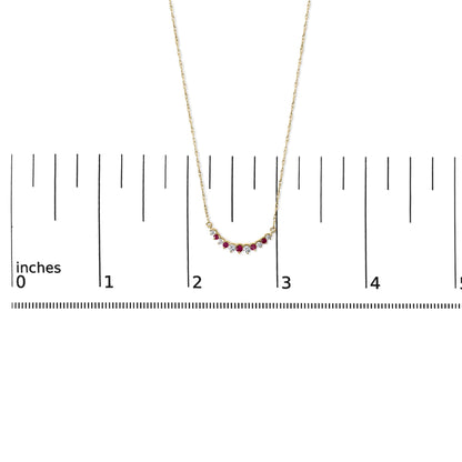 Yellow metal necklace with a curved pendant featuring round red and white gemstones in prong settings, shown on a ruler scale from front angle.