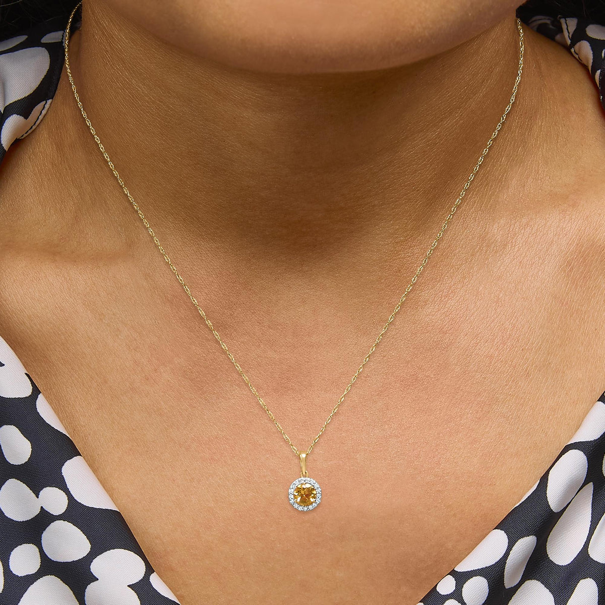 Yellow metal necklace with a round yellow gemstone pendant surrounded by white gemstones in prong settings, shown worn on a model, close-up front view.