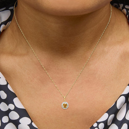 Yellow metal necklace with a round yellow gemstone pendant surrounded by white gemstones in prong settings, shown worn on a model, close-up front view.