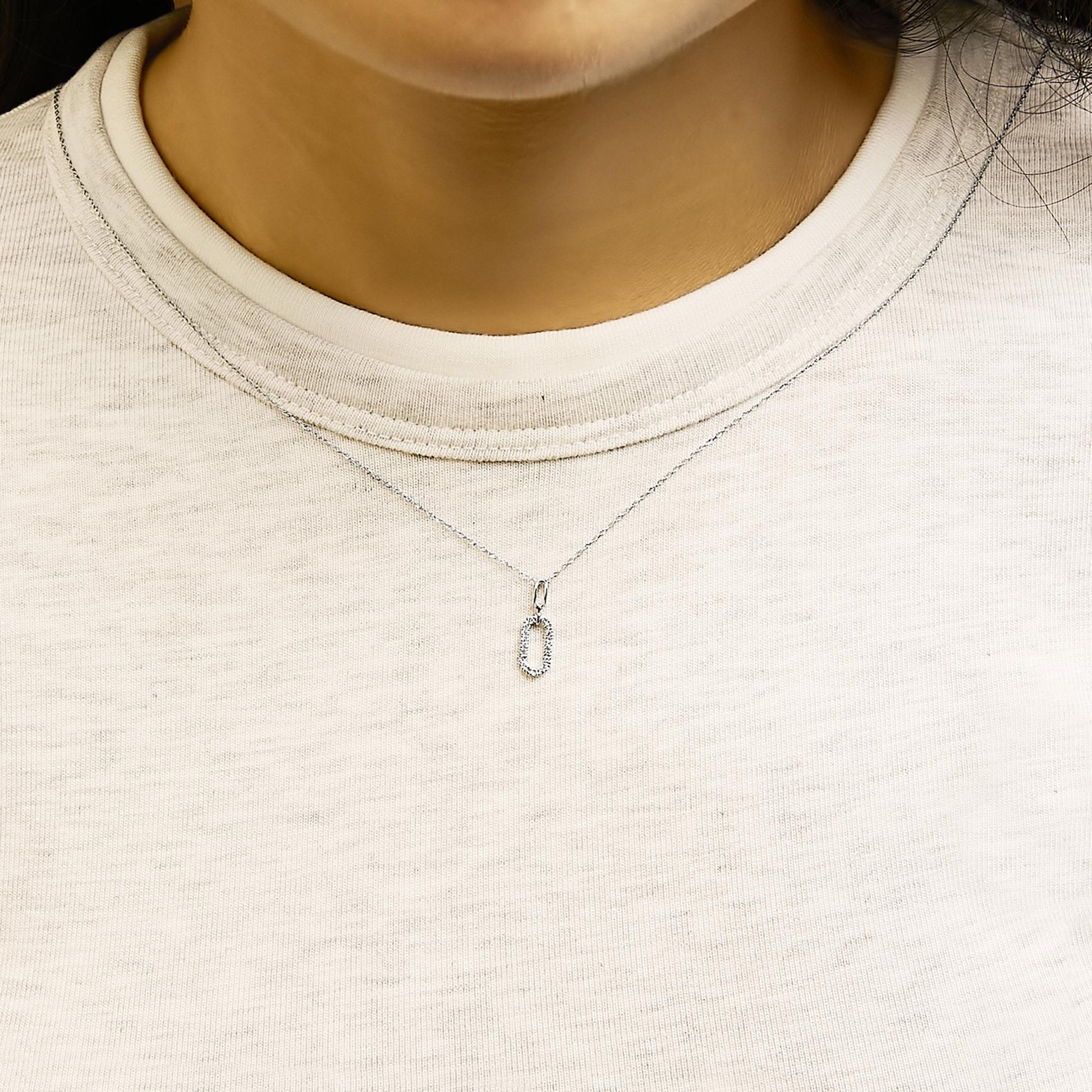 Close-up front view of a model wearing a white metal necklace with a small rectangular pendant set with round white gemstones in a pave setting.