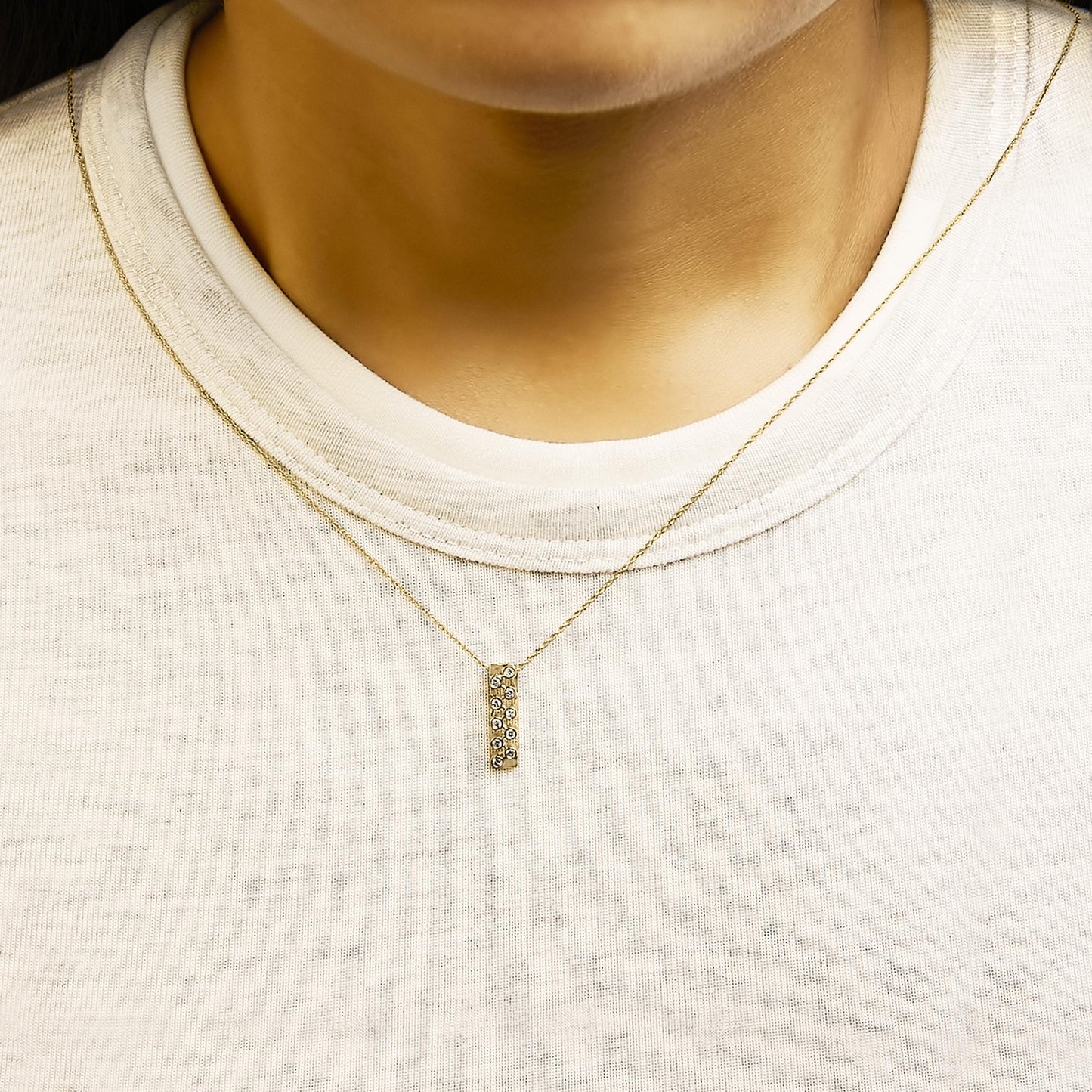 Close-up front view of a yellow metal necklace with a vertical rectangular pendant featuring round white gemstones in bezel settings, shown worn on a model.