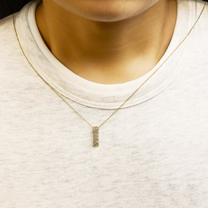 Close-up front view of a yellow metal necklace with a vertical rectangular pendant featuring round white gemstones in bezel settings, shown worn on a model.