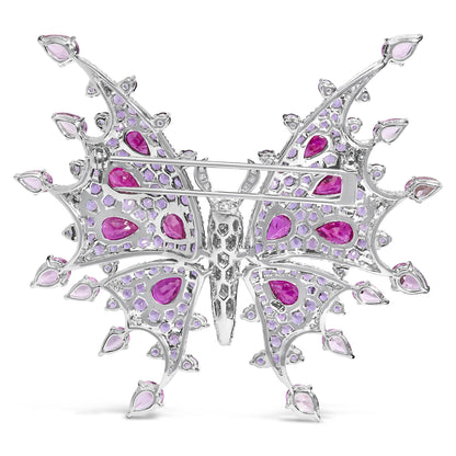 Back view of a white butterfly-shaped brooch with red pear-shaped gemstones, pink pear-shaped gemstones, purple round gemstones, and white round gemstones in pave setting, shown flat on a white background.