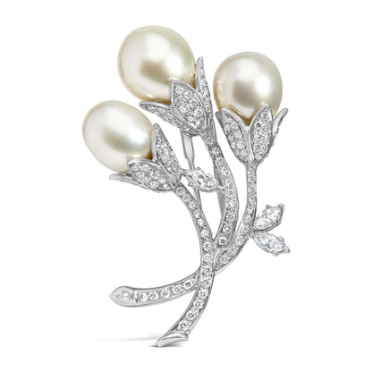 White metal brooch shaped like three flower buds with white round pave-set gemstones on stems and leaves, and three large pearl-like accents, shown from a front angle.