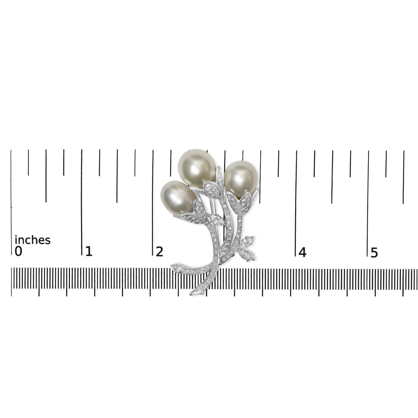 White metal brooch with three oval pearl-like elements and pavé-set round white gemstones on leaf and stem design, pictured from above on a ruler for size reference.