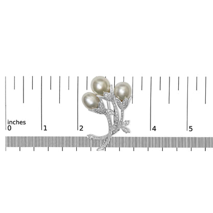 White metal brooch with three oval pearl-like elements and pavé-set round white gemstones on leaf and stem design, pictured from above on a ruler for size reference.