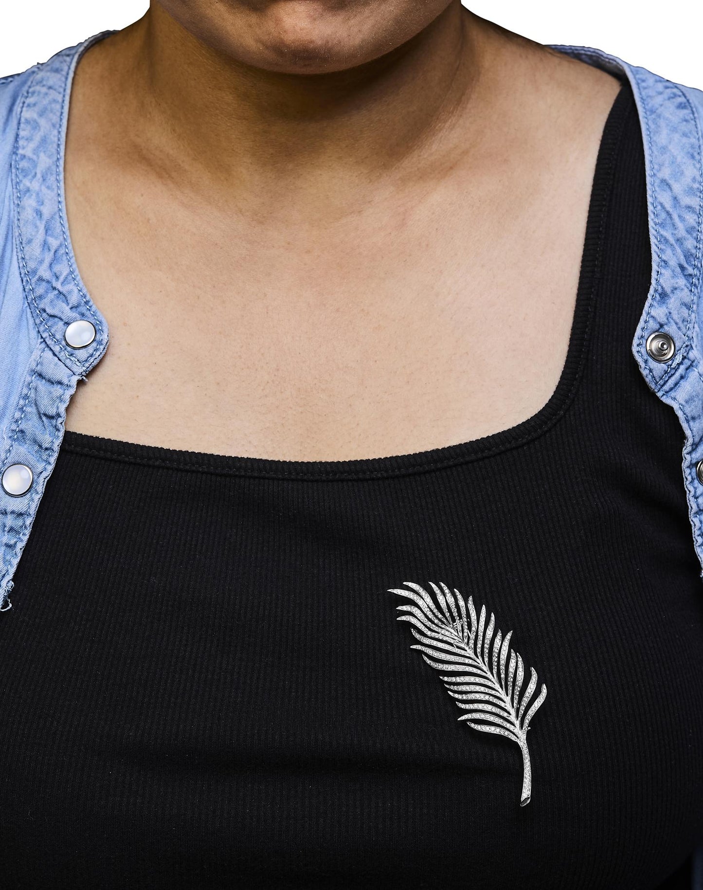 Brooch in the shape of a leaf with white gemstones in pave setting, worn on a model's black top, front-facing angle.