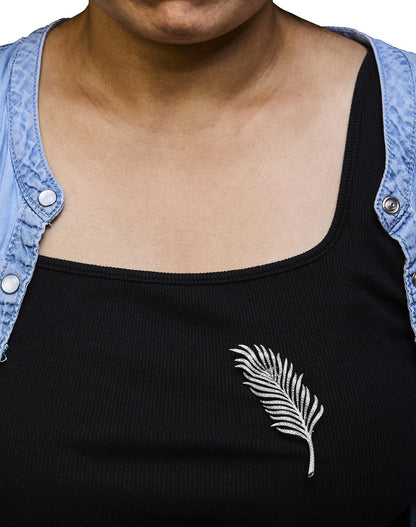 Brooch in the shape of a leaf with white gemstones in pave setting, worn on a model's black top, front-facing angle.