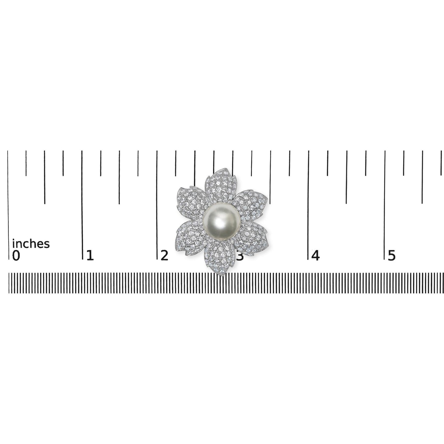 Top-down view of a white metal flower-shaped brooch with a central smooth round white gemstone and petals encrusted with small round white gemstones in pave setting, placed on a ruler for size reference.