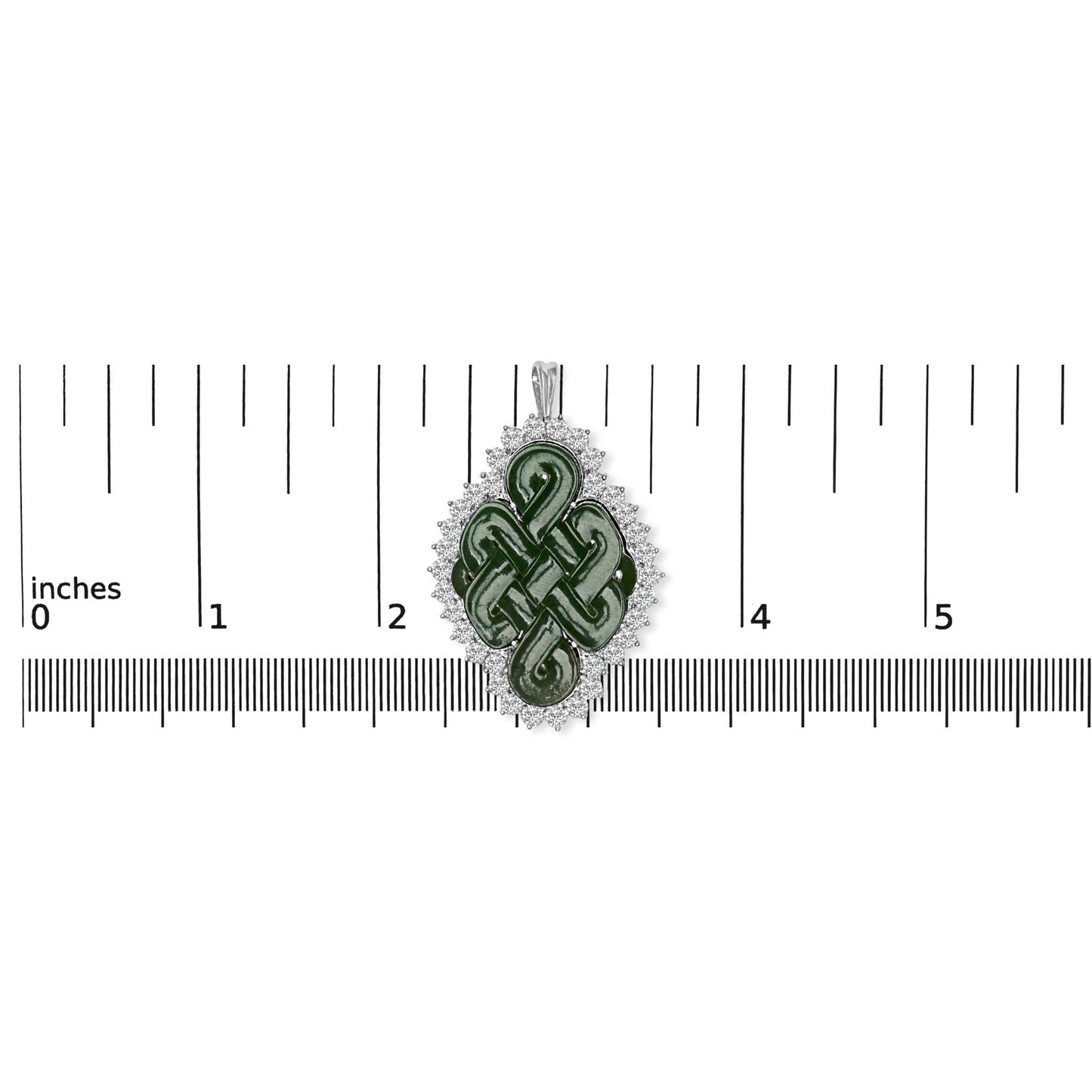 Top-down view of a white metal brooch with a green fantasy-shaped gemstone in the center, surrounded by a border of round white gemstones, placed on a ruler for size reference.
