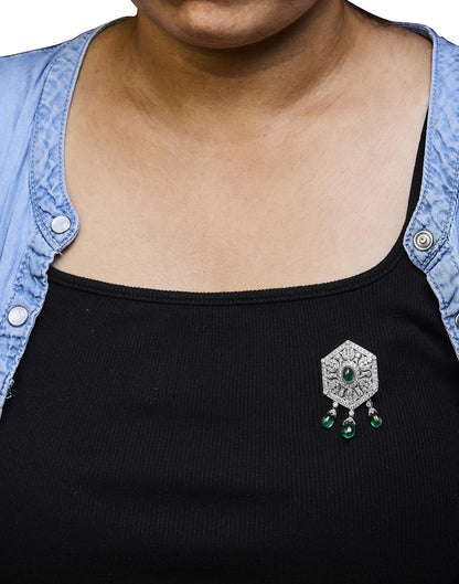 Brooch with white metal and intricate design featuring round and marquise white gemstones, and fantasy and oval green gemstones, worn on a model shown from the front angle.