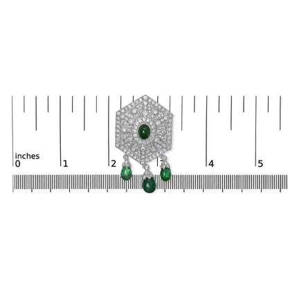Top-down view of a white brooch with round and marquise shaped white gemstones in pave and prong settings, featuring a central oval green gemstone and three dangling green fantasy-shaped gemstones, placed on a ruler for size reference.