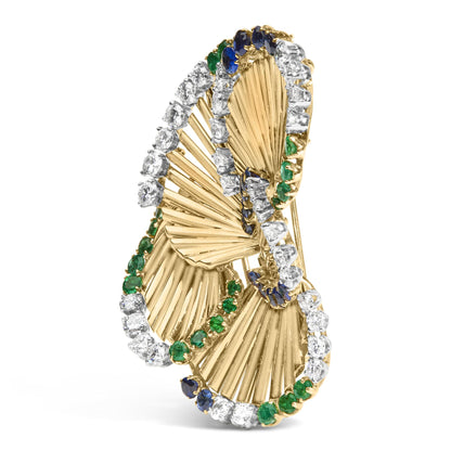 Yellow metal brooch with three overlapping fan shapes outlined with white, blue, and green gemstones, shown at a slight side angle.