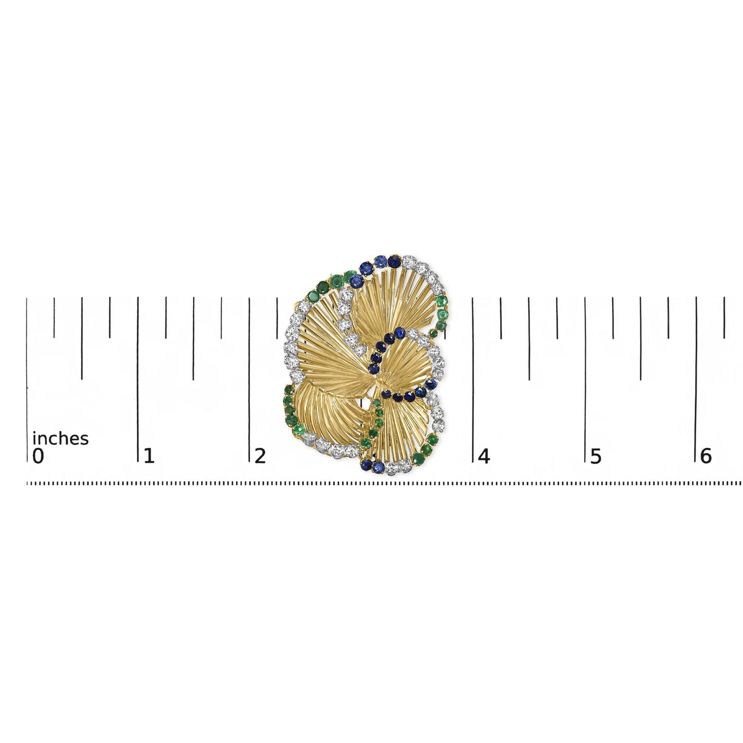 Yellow metal brooch with textured fan-like shapes, accented with round white, blue, and green gemstones in four-prong settings, shown on a ruler for size reference, top-down angle.
