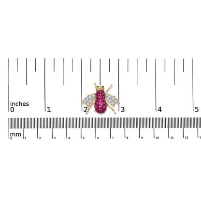 Top-down view of a yellow metal insect-shaped brooch with red gemstones on the body, white gemstones on the wings, and green gemstones on the eyes, placed on a ruler for size reference.