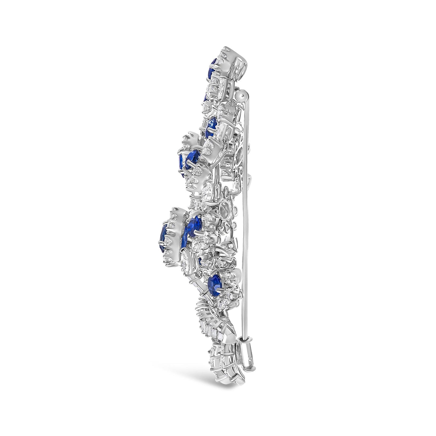 Side view of a white metal brooch with prong-set white gemstones in marquise, pear, round, and baguette shapes, and oval blue gemstones, shown standing upright.