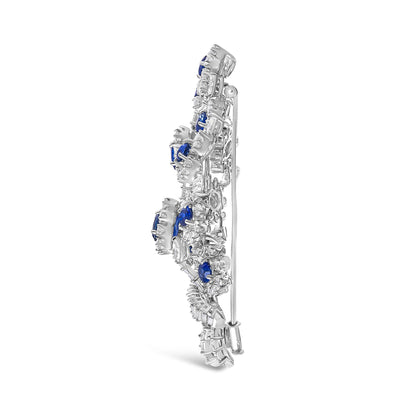 Side view of a white metal brooch with prong-set white gemstones in marquise, pear, round, and baguette shapes, and oval blue gemstones, shown standing upright.