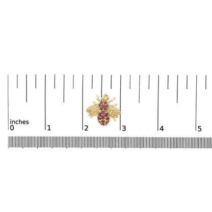 Yellow metal brooch in the shape of a bee with red round gemstones, shown on a scale from above.