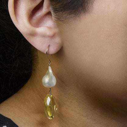 Side view of a yellow metal earring with an irregular white gemstone and a yellow gemstone hanging below, worn on a model.
