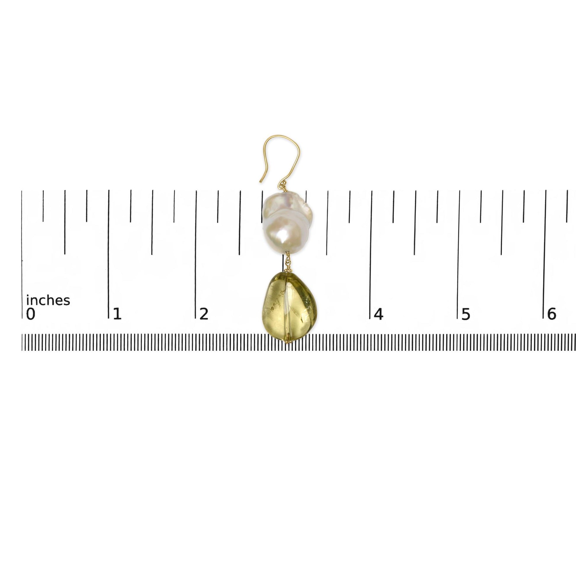 Single yellow metal earring with irregular yellow gemstone and baroque white gemstone, shown on a ruler for size reference, top-down view.