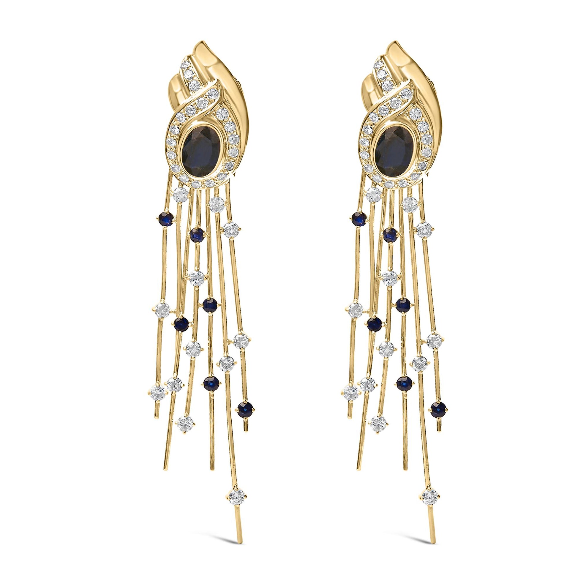 Pair of yellow metal earrings shown from the front, featuring an oval blue gemstone in a bezel setting surrounded by a swirl of white gemstones in a pave setting, with multiple thin strands dangling below adorned with round blue and white gemstones in prong settings.