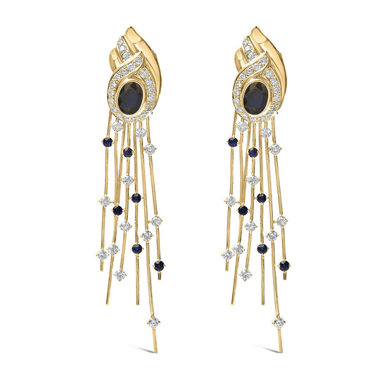 Pair of yellow metal earrings shown from the front, featuring an oval blue gemstone in a bezel setting surrounded by a swirl of white gemstones in a pave setting, with multiple thin strands dangling below adorned with round blue and white gemstones in prong settings.