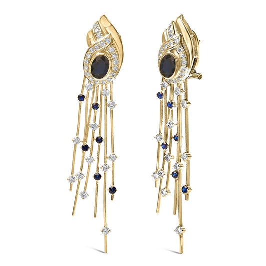 Pair of yellow metal long dangling earrings with oval blue gemstones in bezel settings surrounded by curved lines of small white gemstones, with multiple thin strands hanging down adorned with small round blue and white gemstones, shown from a front angle.