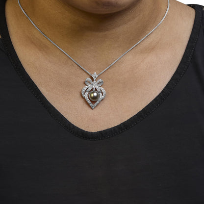 Close-up front view of a white metal necklace on a model, featuring a pendant with a bow-shaped design adorned with white gemstones in pave setting and a central dark round gemstone.
