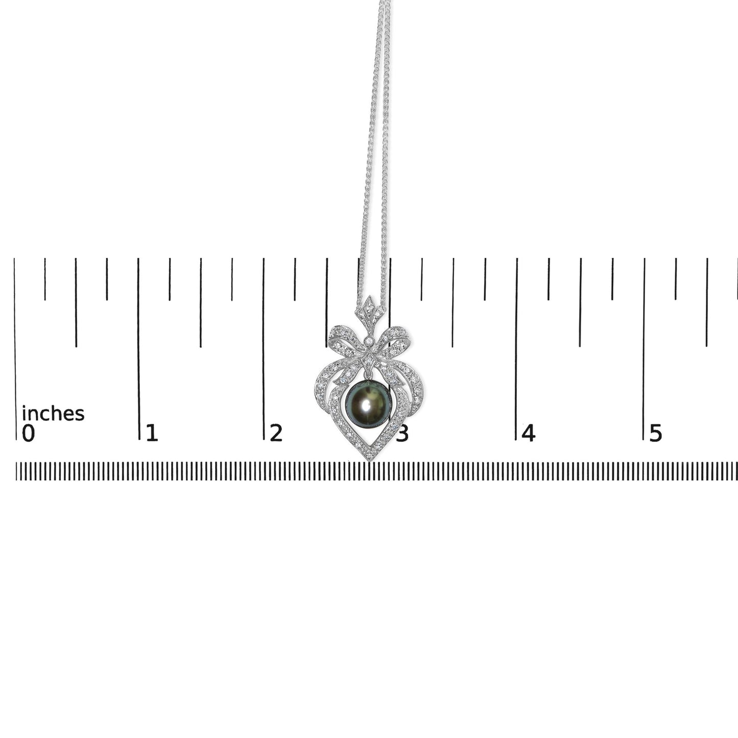 White metal necklace with heart-shaped pendant adorned with pave-set round white gemstones and a central dark gemstone, shown hanging against a ruler for size reference, front-facing angle.