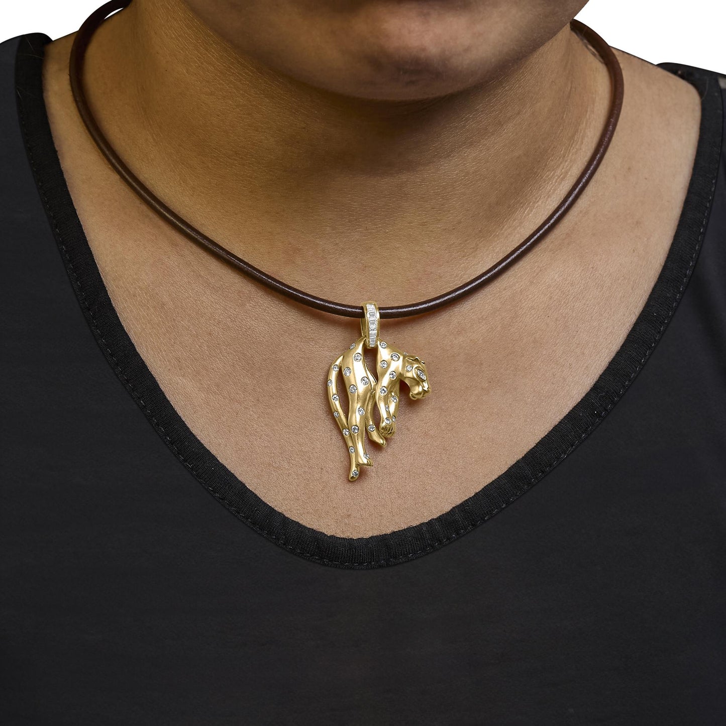 Close-up front view of a yellow metal necklace with a pendant shaped like a stylized animal head adorned with small white round gemstones, two marquise-shaped white gemstones in bezel setting, one princess-shaped gemstone and several baguette-shaped gemstones in channel setting, worn on a model with a dark top.