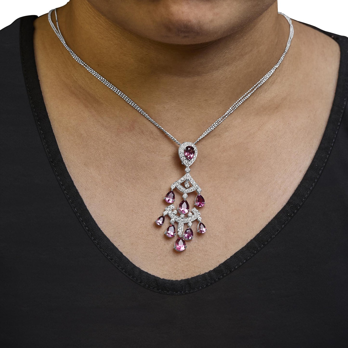 Close-up, front view of a white metal necklace worn on a model, featuring a pendant with a combination of round white gemstones and pear-shaped pink gemstones in prong settings.