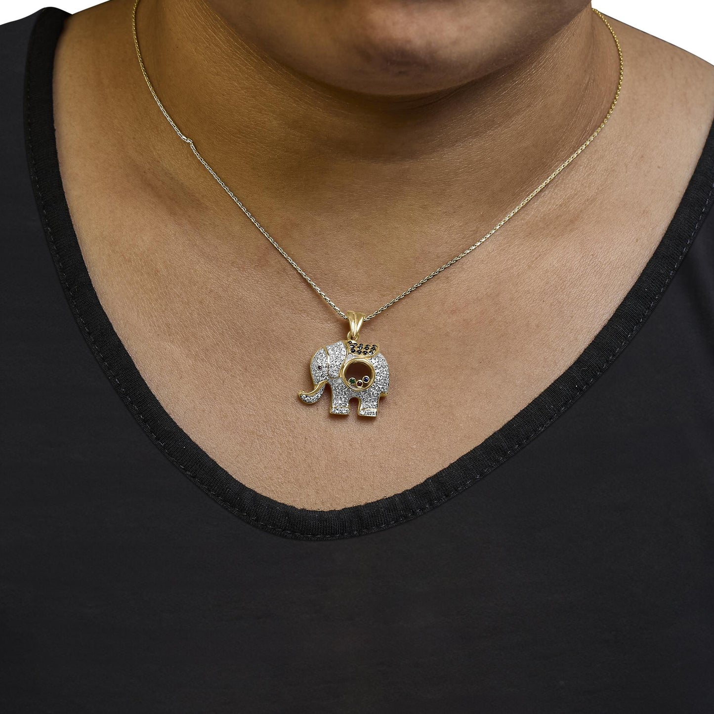 Yellow metal necklace with an elephant-shaped pendant featuring numerous white gemstones in pave setting, blue gemstones in pave setting, and a few bezel-set red and green gemstones, shown on a model from the front angle.