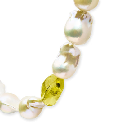 Close-up angled view of a yellow metal necklace featuring irregularly shaped white pearls and a yellow translucent gemstone in a drilled setting.