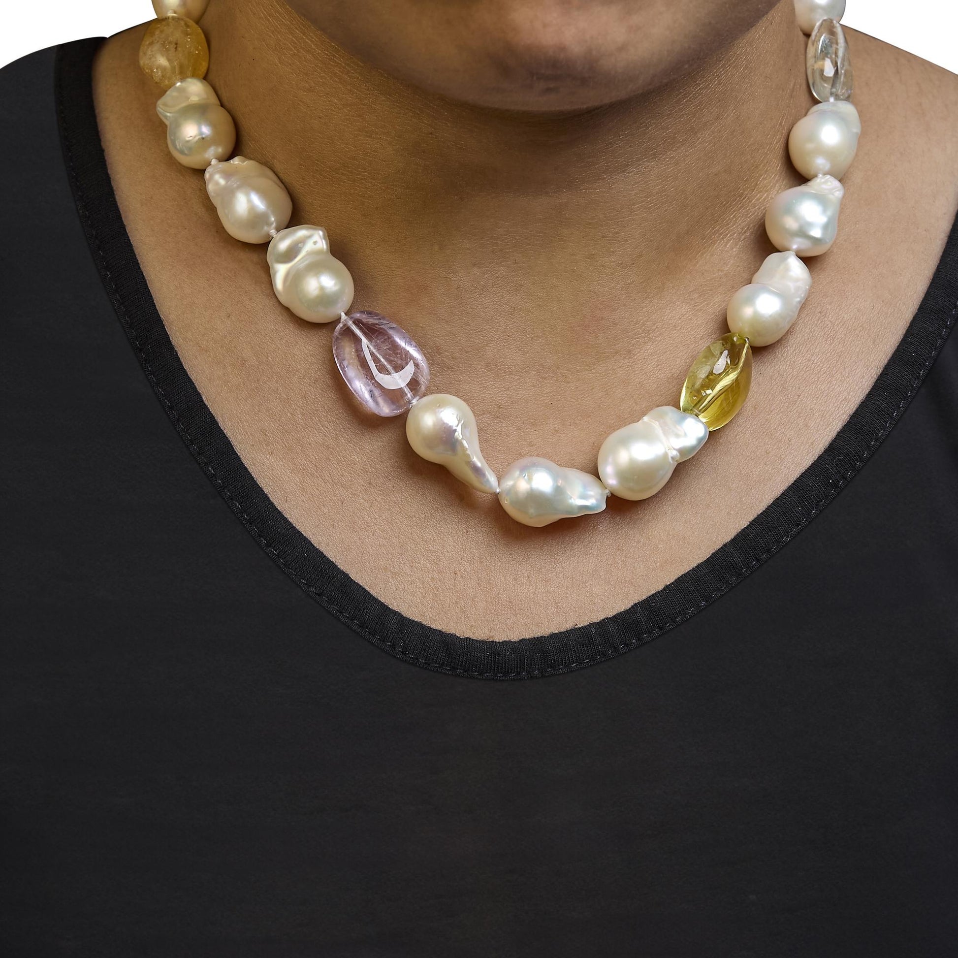 Close-up front view of a necklace on a model featuring irregular white pearls and yellow oval-shaped drilled gemstones.