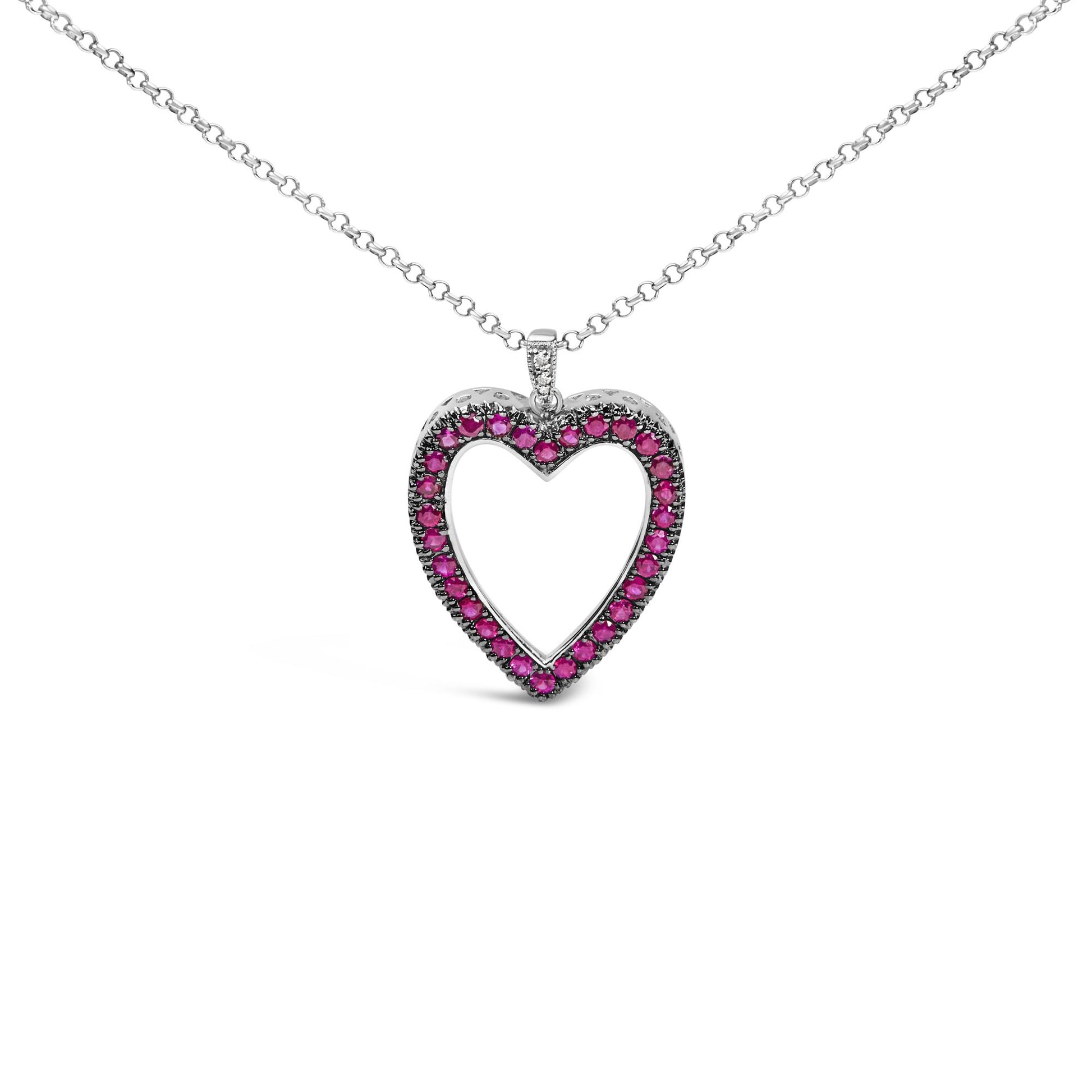 Front-facing shot of a white metal heart-shaped necklace pendant adorned with round red gemstones in shared prong setting and a few round white gemstones in pave setting on the bail.