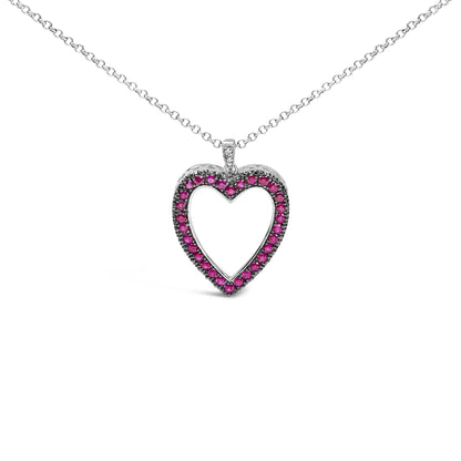 Front-facing shot of a white metal heart-shaped necklace pendant adorned with round red gemstones in shared prong setting and a few round white gemstones in pave setting on the bail.