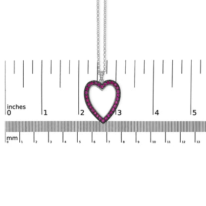 White metal heart-shaped necklace pendant with round red gemstones along the border and three small round white gemstones at the top, shown hanging against a ruler for size reference, front-facing angle.