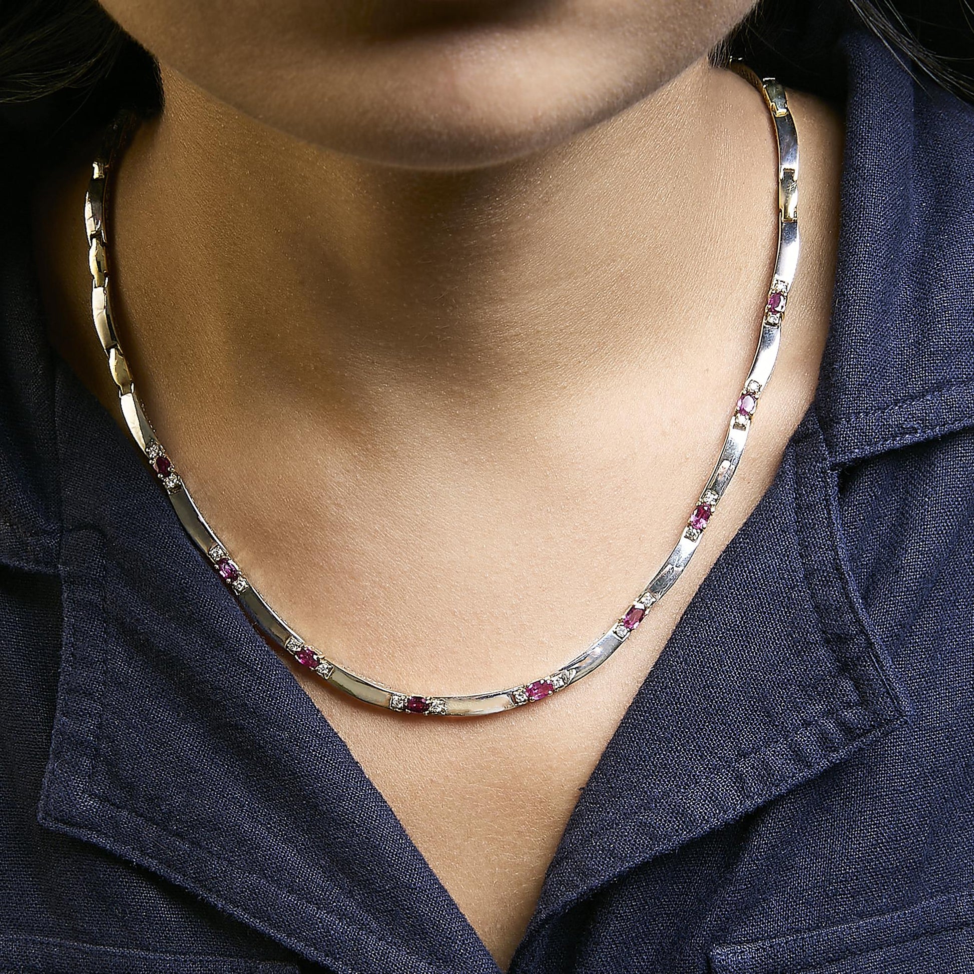 Necklace with alternating yellow and white metal links set with oval red gemstones and round white gemstones, shown worn on a model from the front angle.