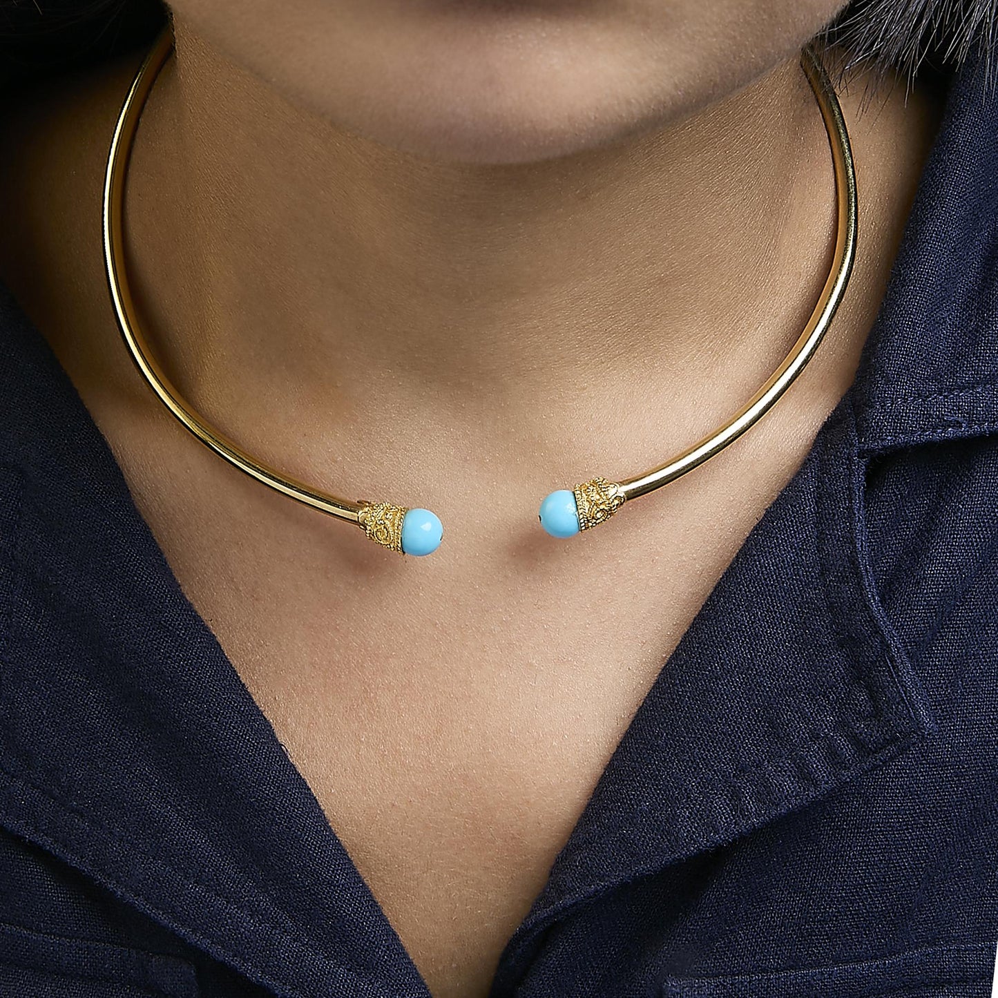 Close-up front view of a yellow metal open choker necklace with round blue gemstones on each end, shown worn on a model.