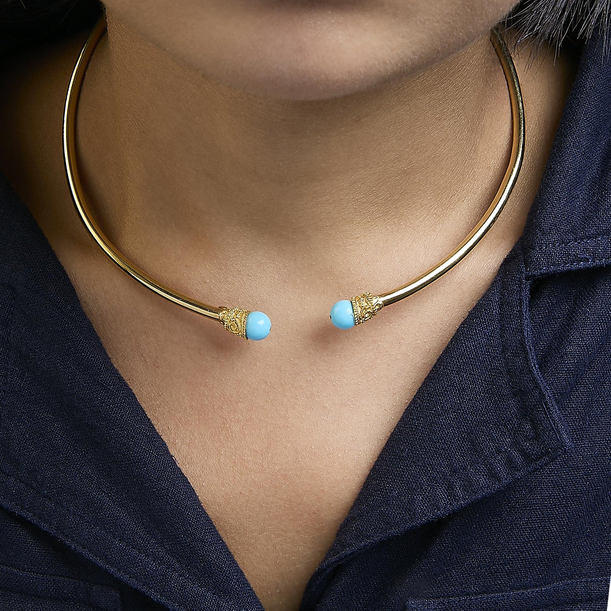 Close-up front view of a yellow metal open choker necklace with round blue gemstones on each end, shown worn on a model.