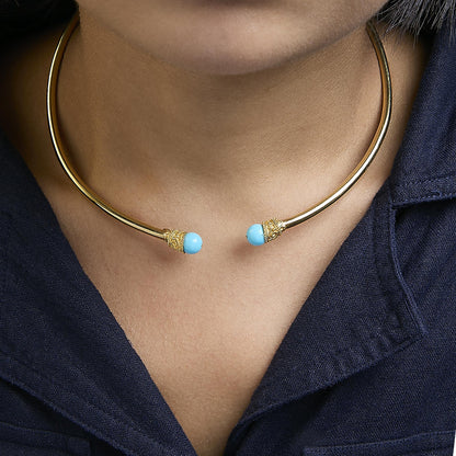 Close-up front view of a yellow metal open choker necklace with round blue gemstones on each end, shown worn on a model.
