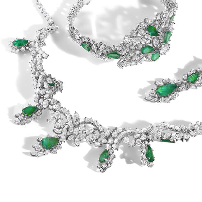 Set of jewelry pieces displayed in a flat lay, featuring white metal adorned with pear-shaped green gemstones and variously shaped white gemstones, including round, marquise, and baguette cuts, arranged in intricate patterns.