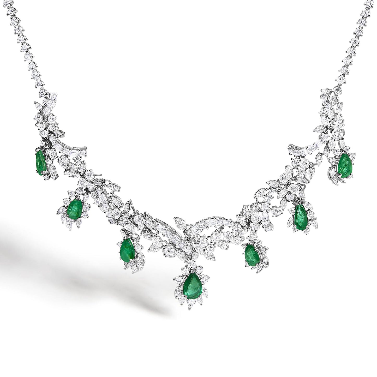 Close-up front angle of a white metal necklace set featuring intricate design with round, baguette, and marquise shaped white gemstones, accented with pear-shaped green gemstones evenly spaced along the piece.