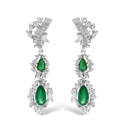 Pair of white metal drop earrings with pear-shaped green gemstones surrounded by various round and marquise-shaped white gemstones, shown from a front angle on a white background.